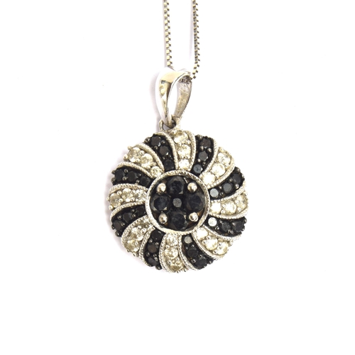 63 - A 14ct white gold pendant set with black and white diamonds in a swirl design, 15cm diameter, on a 1... 