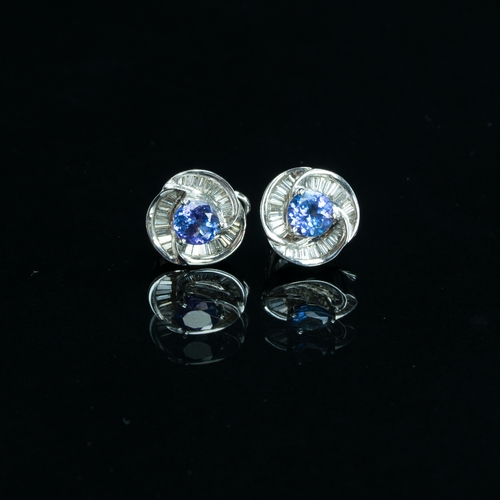 91 - A pair of heavy 18ct white gold earrings set with a central tanzanite, 6.5mm diameter, surrounded by... 