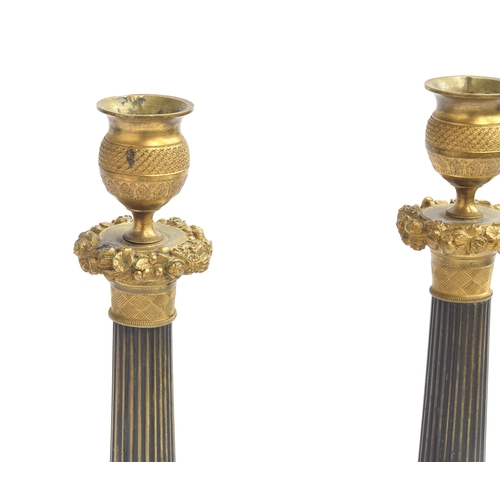 89 - A pair of 19th century French patinated bronze and ormolu mounted candlesticks, the gilded drip pan ... 