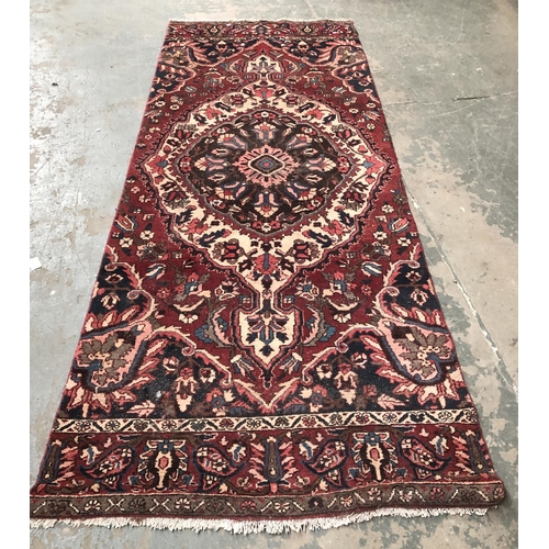 978 - A Persian wool rug, blue and burgundy with central lozenge, approx 303x127cm