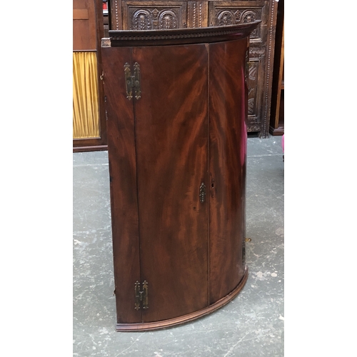 712 - A George III bowfront mahogany corner cupboard, opening to a painted interior with three shelves, 10... 