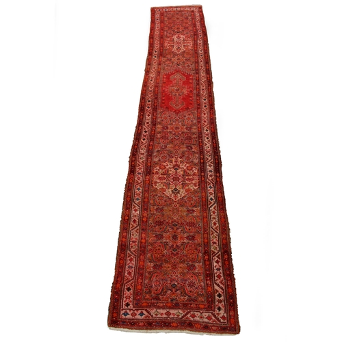 486 - A mid to late 20th century middle Eastern red and orange ground runner, with a multiple banded borde... 