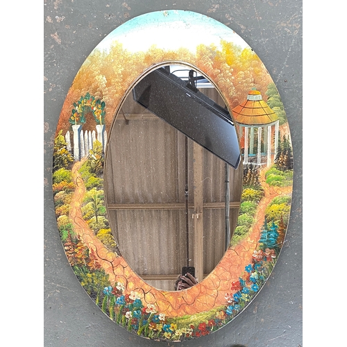 814 - An oval mirror in painted frame, depicting a garden path with pavilion and arch, 92x67cm