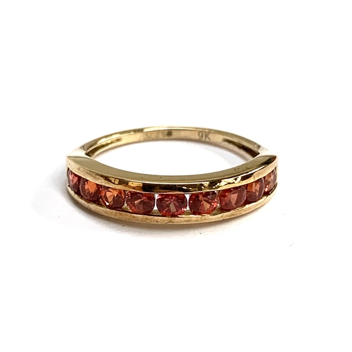 64 - A 9ct gold half eternity ring channel set with reddish orange sapphires, size P. 2.2g