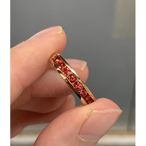 64 - A 9ct gold half eternity ring channel set with reddish orange sapphires, size P. 2.2g