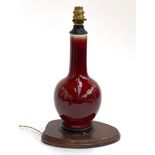 192 - A porcelain red glazed sang de boeuf vase of bottle form, converted to a lamp, on a wooden base, the... 