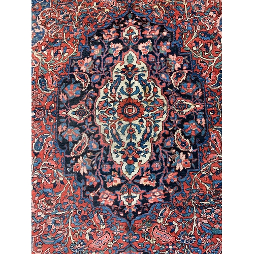 799 - A red ground rug with blue and red floral rectangle, ovoid centre, 215x302cm