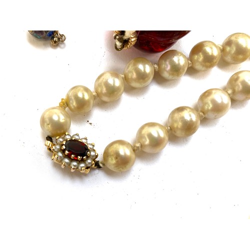 24 - A quantity of faux pearl necklaces, one fastening with a yellow metal, garnet and split pearl clasp;... 