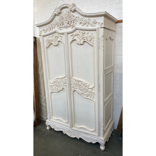 1061 - A large white painted Continental style hanging wardrobe with floral carved pediment and drawers, 12... 