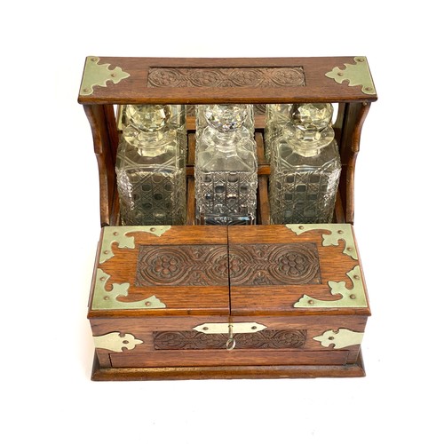 172 - An early 20th century Betjemann style oak tantalus with white metal mounts and floral carved detail,... 