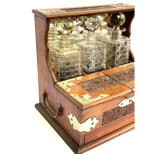 172 - An early 20th century Betjemann style oak tantalus with white metal mounts and floral carved detail,... 