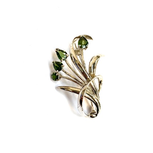 32 - A white metal brooch in the form of a floral spray set with four pear shaped green sapphires, the la... 