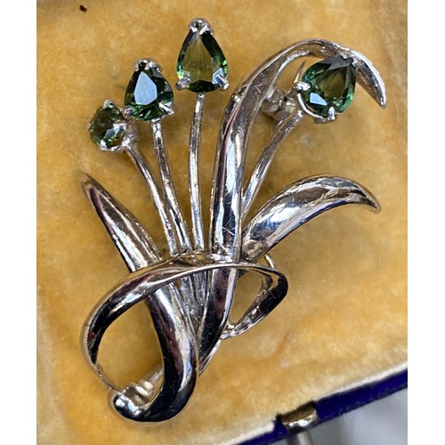 32 - A white metal brooch in the form of a floral spray set with four pear shaped green sapphires, the la... 