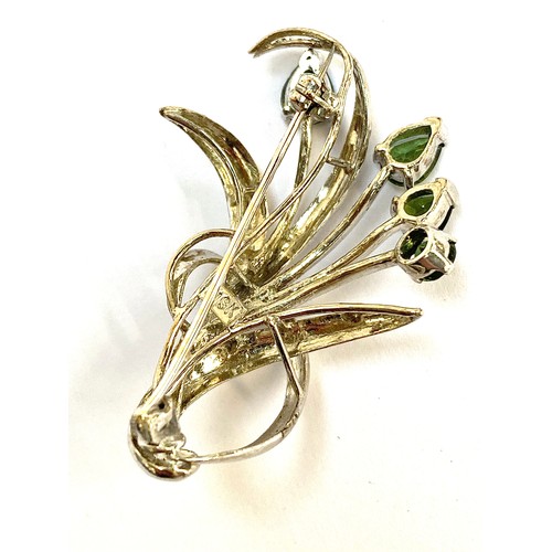 32 - A white metal brooch in the form of a floral spray set with four pear shaped green sapphires, the la... 