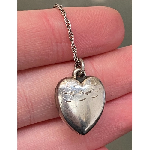 35 - An early 20th century silver puffy heart pendant on a silver chain, the heart with engraved detail, ... 