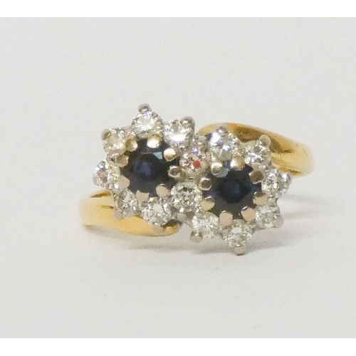 695 - A sapphire and diamond double cluster cross over design dressing, in 18ct gold, ring size L