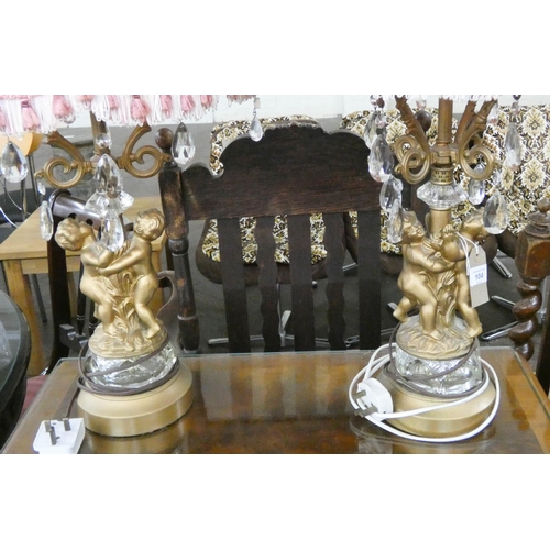 104 - A pair of gilt and glass decorative cherub table lamps with lustres and pink shades