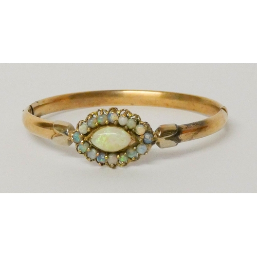 649 - A gold and opal bangle, with a central oval opal cluster, measuring 2.5 cms across.  Weight 11 grams