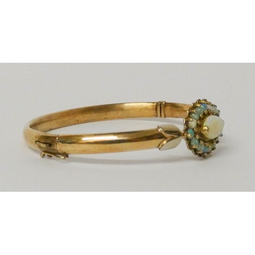 649 - A gold and opal bangle, with a central oval opal cluster, measuring 2.5 cms across.  Weight 11 grams