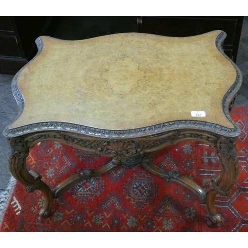 352 - A shaped figured walnut coffee table with carved frieze and cross stretcher base