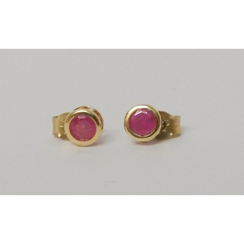 585 - Pair of ruby circular ear studs, on 9ct gold rub over settings and gold posts.