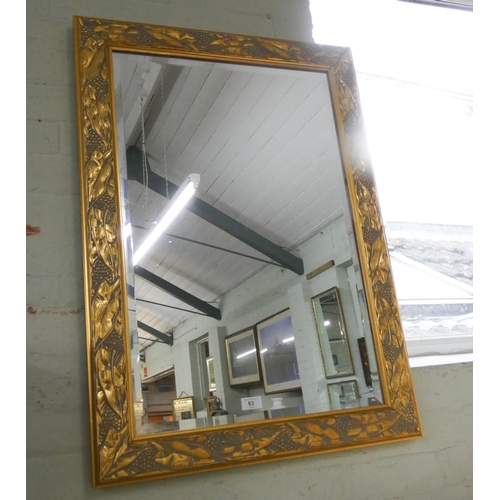 63 - A bevelled wall mirror in leaf patterned decorative gilt frame