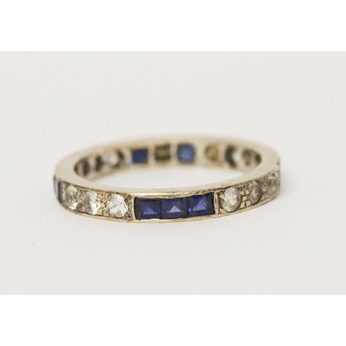 654 - A sapphire and white stone full eternity ring, unmarked white metal. Ring size M