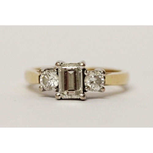 734 - A three stone diamond ring, with central emerald cut diamond flanked by princess cut diamonds, on 18... 