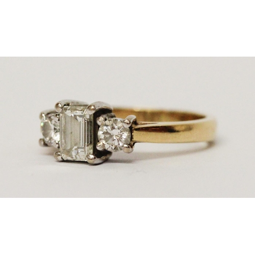 734 - A three stone diamond ring, with central emerald cut diamond flanked by princess cut diamonds, on 18... 