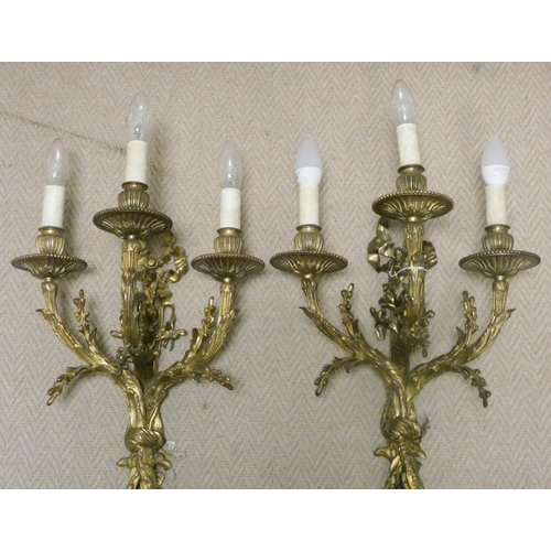 302 - A pair of early 20th century gilt brass three branch wall sconces, wired for electricity, overall le... 