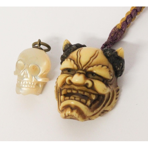 612 - Japanese carved bone devil mask toggle/ pendant and a carved mother of pearl skull pendant.