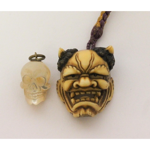 612 - Japanese carved bone devil mask toggle/ pendant and a carved mother of pearl skull pendant.