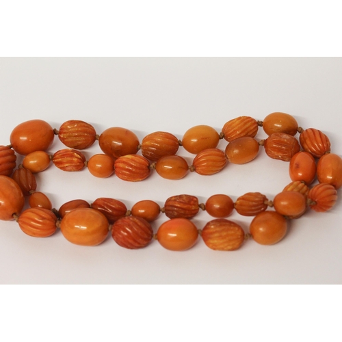 650 - Long vintage row of amber beads, the row individually knotted of oval carved and plain beads. Weight... 