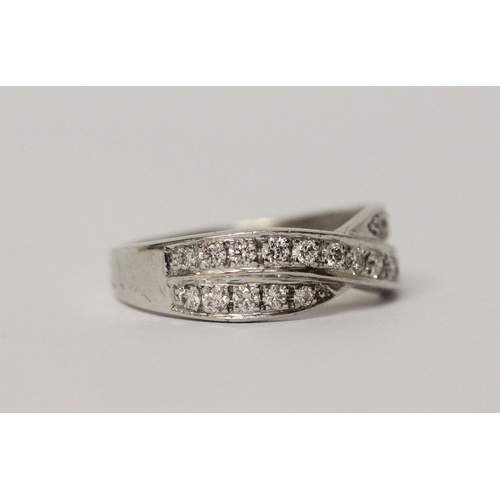 506 - A diamond channel set cross over design band ring. On unmarked white precious metal. Ring size K, we... 