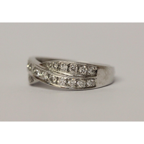 506 - A diamond channel set cross over design band ring. On unmarked white precious metal. Ring size K, we... 