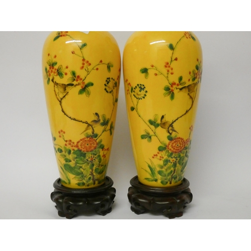 177 - A pair of Chinese yellow bird and floral decorated vases with wooden stands, 11 1/4