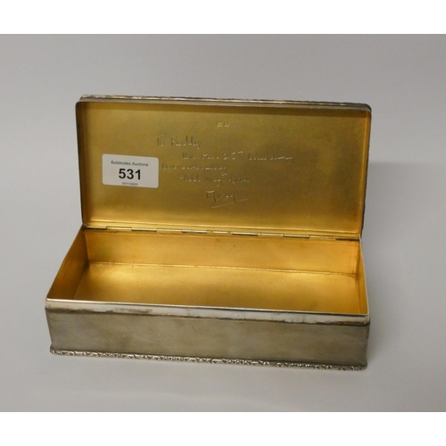 531 - A silver cigarette box, with engine turned detail and cast edge, the hinged lid with gilded interior... 