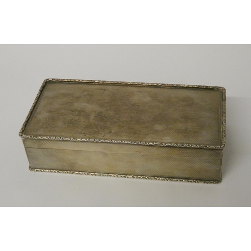 531 - A silver cigarette box, with engine turned detail and cast edge, the hinged lid with gilded interior... 