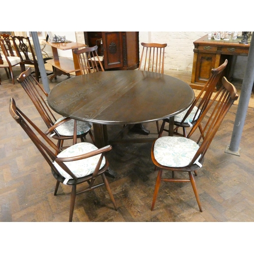 140 - An Ercol dark oak drop leaf dining table and a set of six stick back Windsor style chairs comprising... 