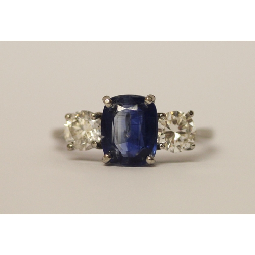 454 - A sapphire and diamond three stone ring, The central oval mixed cut sapphire claw set, flanked betwe... 