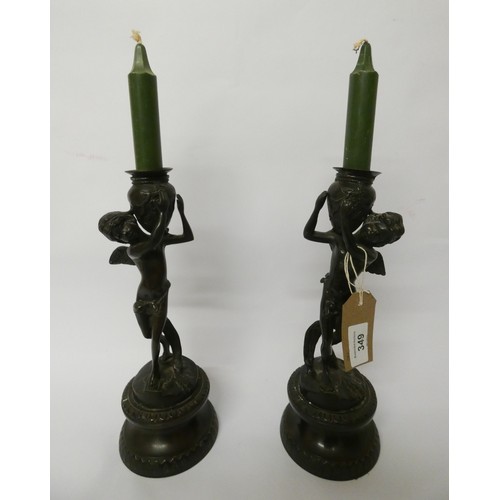 349 - A pair of bronze cherub candlesticks standing on circular bases, each standing 28cms tall