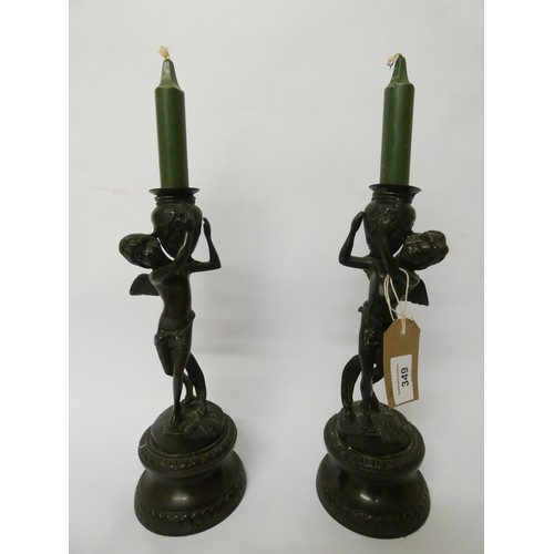 349 - A pair of bronze cherub candlesticks standing on circular bases, each standing 28cms tall