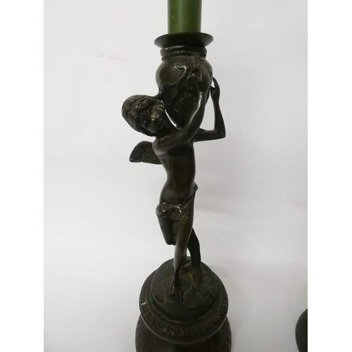 349 - A pair of bronze cherub candlesticks standing on circular bases, each standing 28cms tall