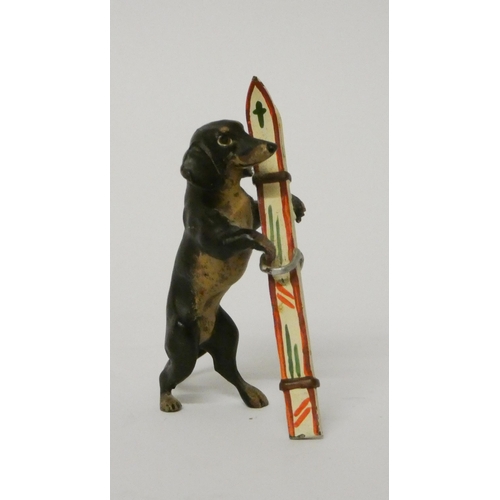 323 - Miniature cold painted novelty bronze of a dachshund carrying skis. 5 cms tall