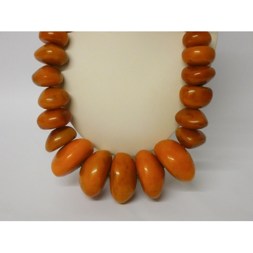 616 - A very large row of amber look beads, largest bead 6cms diameter