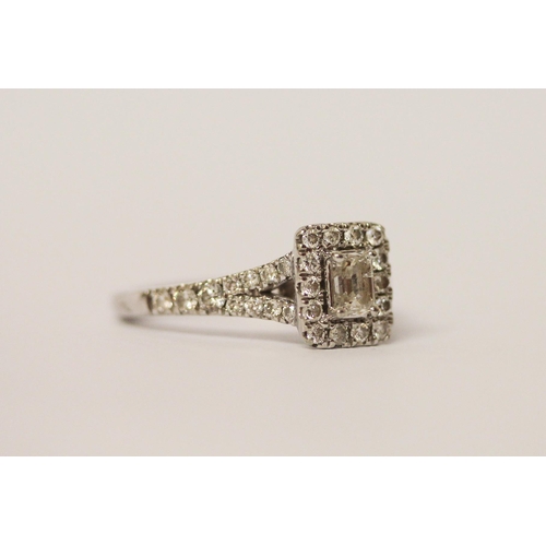 574 - A modern diamond cluster engagement ring, with a central emerald cut diamond surrounded by brilliant... 