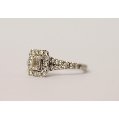 574 - A modern diamond cluster engagement ring, with a central emerald cut diamond surrounded by brilliant... 