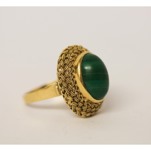 403 - A malachite dress ring, the oval stone in a raised filigree setting on 18ct yellow gold band. Marked... 