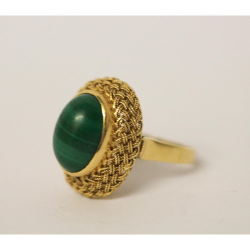 403 - A malachite dress ring, the oval stone in a raised filigree setting on 18ct yellow gold band. Marked... 