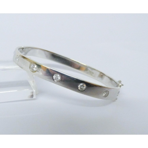 555 - A modern 9ct white gold diamond set hinged bangle, set with seven brilliant cut diamonds, invisible ... 